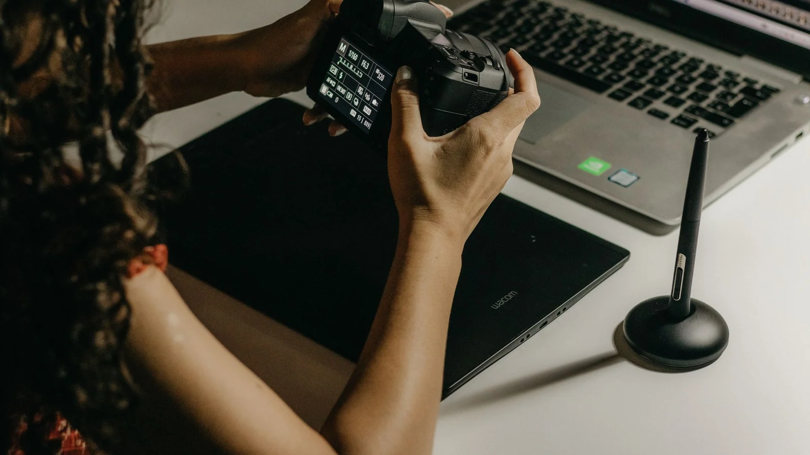 Designer holding a camera beside a laptop and drawing tablet on a desk