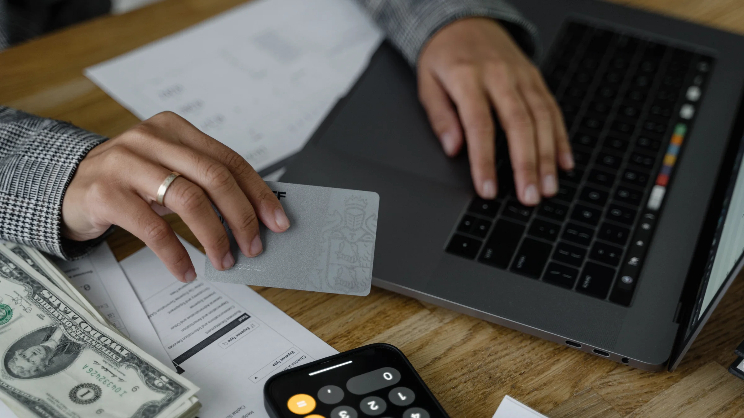 A real work desk scene with a laptop, payment card, calculator, and cash while someone decides whether an AI subscription is worth paying for