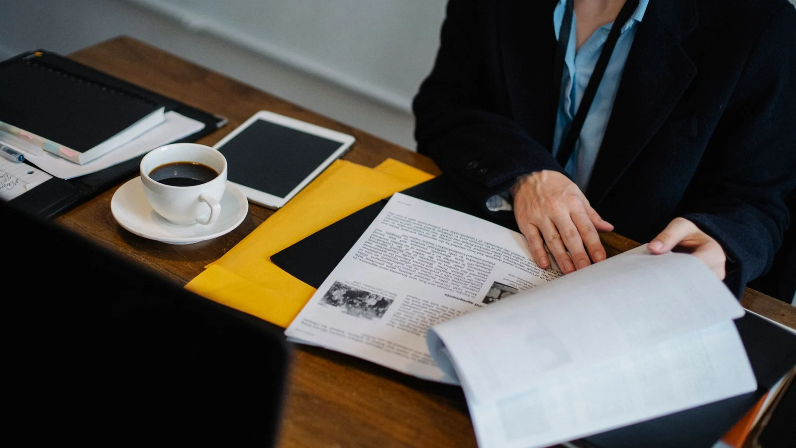 Person reviewing printed documents beside a coffee cup, tablet, and notebook