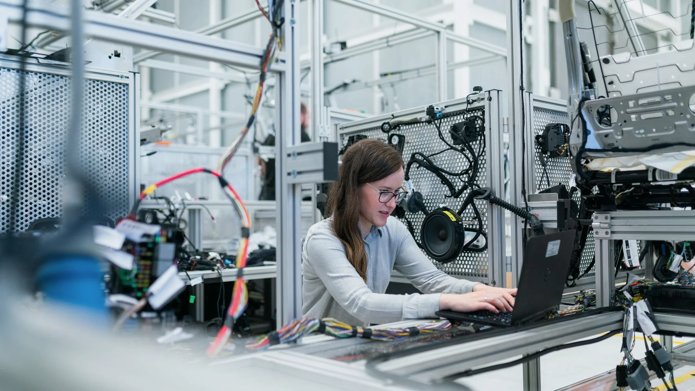 An engineer working on a laptop inside a technical research environment with equipment and wiring around the desk